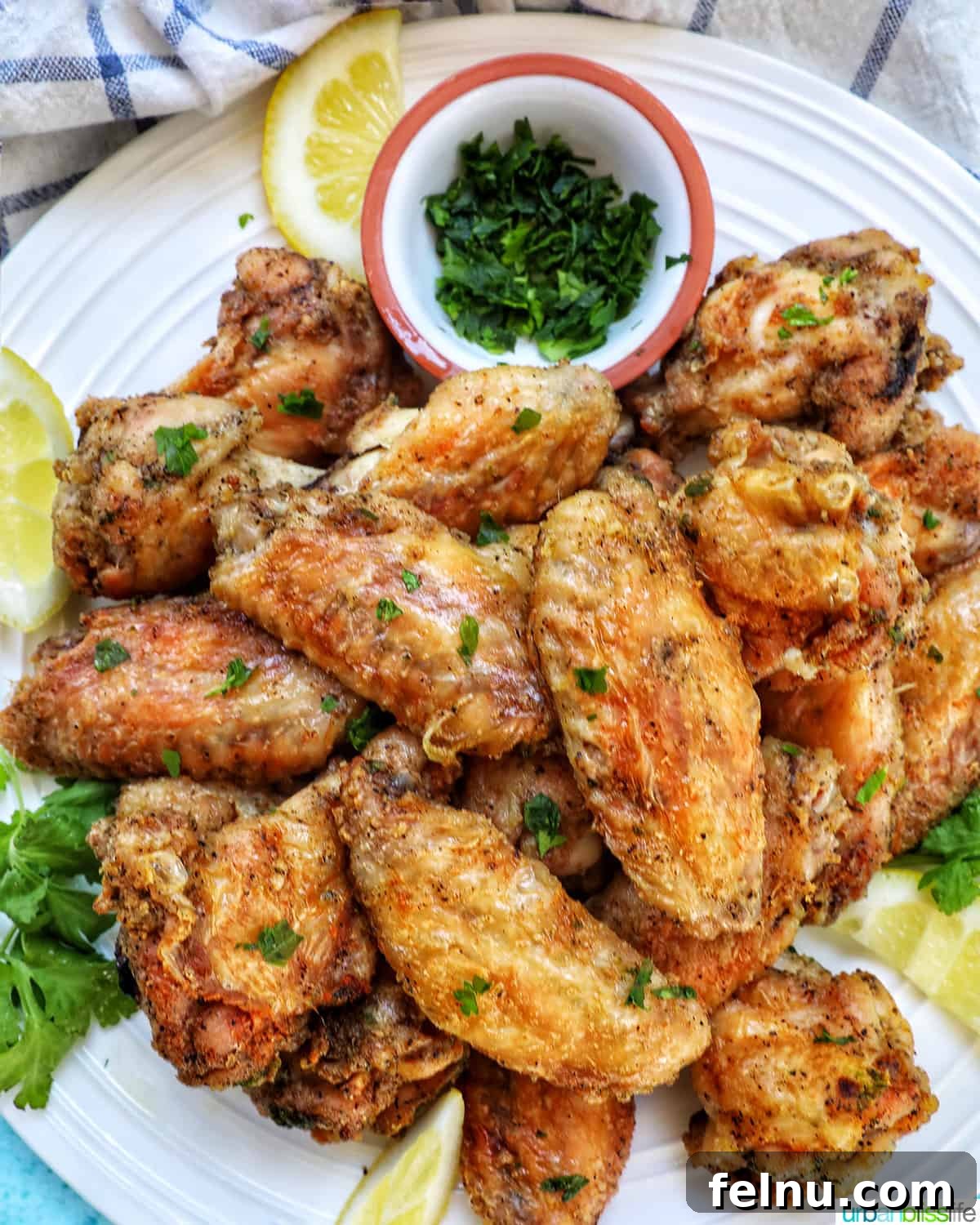 Ultimate Crispy Salt and Pepper Wings 2 white plate full of salt and pepper wings with side of chopped fresh parsley and lemon wedges.