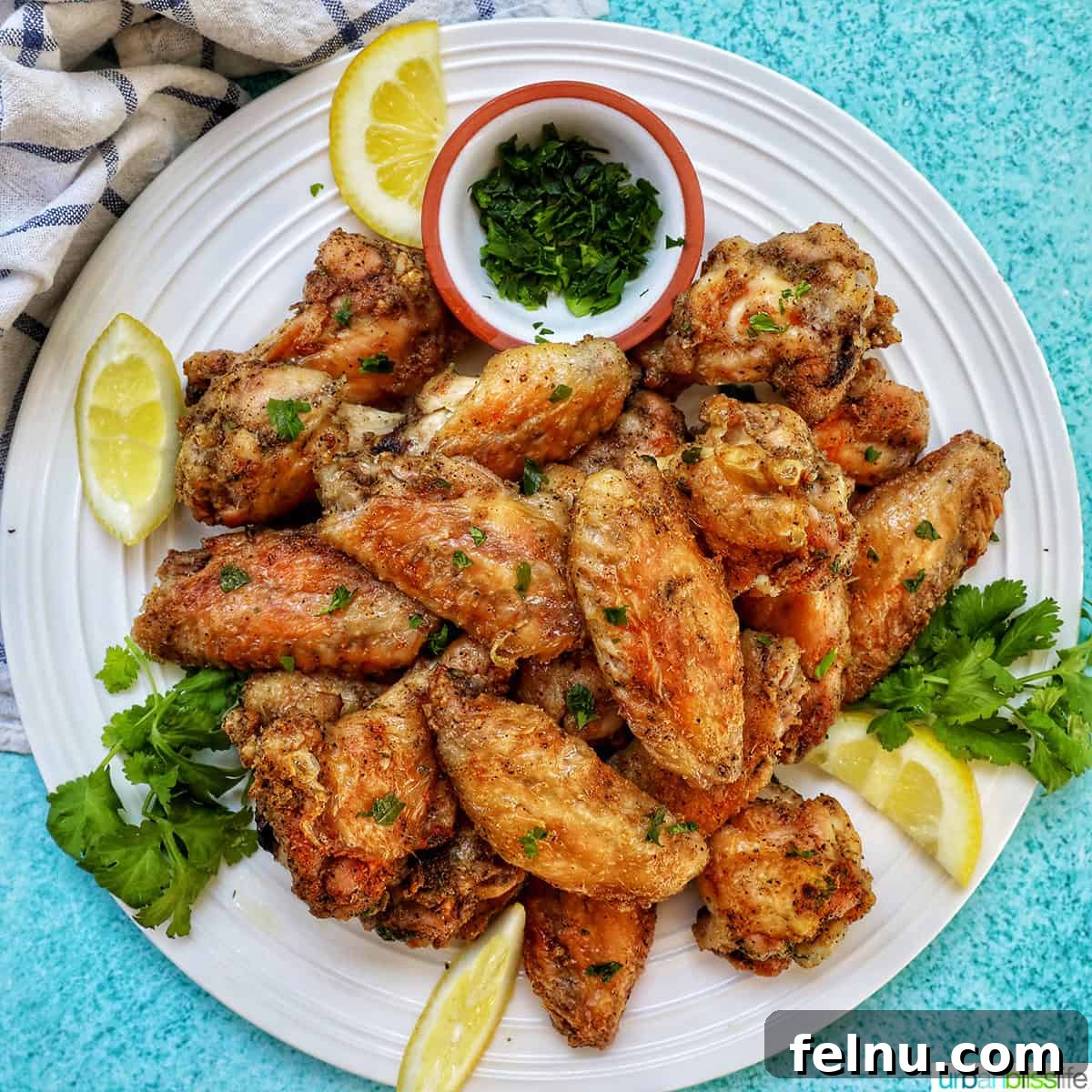 Ultimate Crispy Salt and Pepper Wings 11 white plate full of salt and pepper wings with side of chopped fresh parsley and lemon wedges.