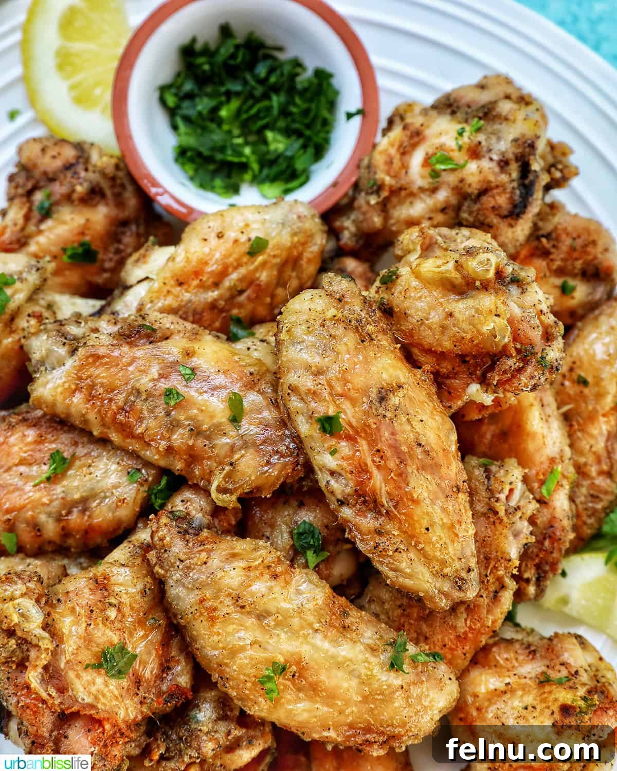 Ultimate Crispy Salt and Pepper Wings 3 white plate full of salt and pepper wings with side of chopped fresh parsley and lemon wedges.
