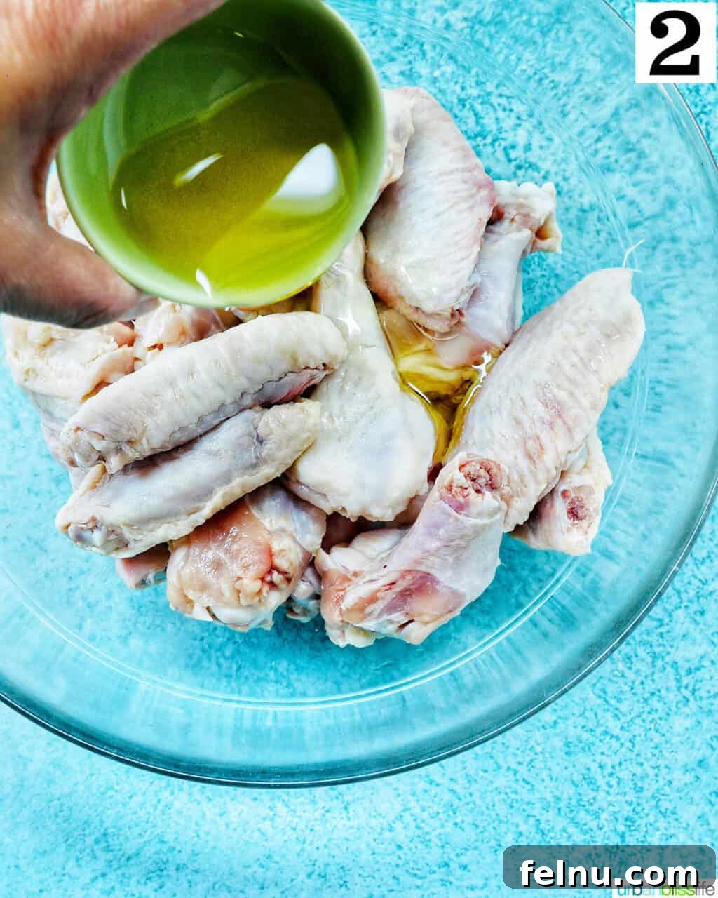 Ultimate Crispy Salt and Pepper Wings 6 hand pouring olive oil over raw chicken wings in a large glass bowl.