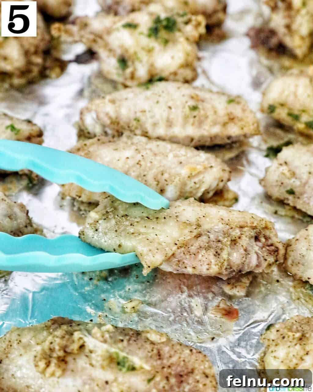Ultimate Crispy Salt and Pepper Wings 9 blue tongs turning over a chicken wing on aluminum foil.