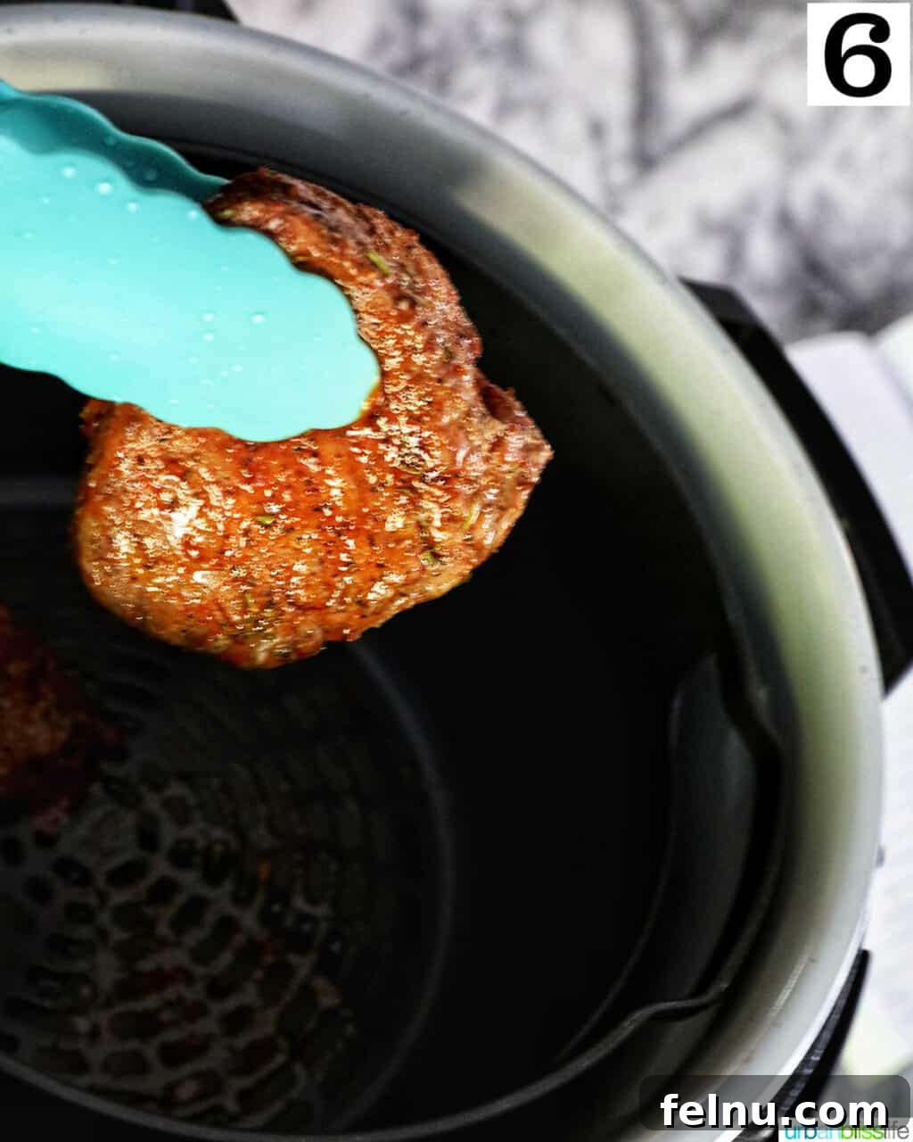 Air Fryer Filet Mignon Perfection 11 blue tongs holding up a half-cooked filet mignon steak over an air fryer basket, ready to be flipped.