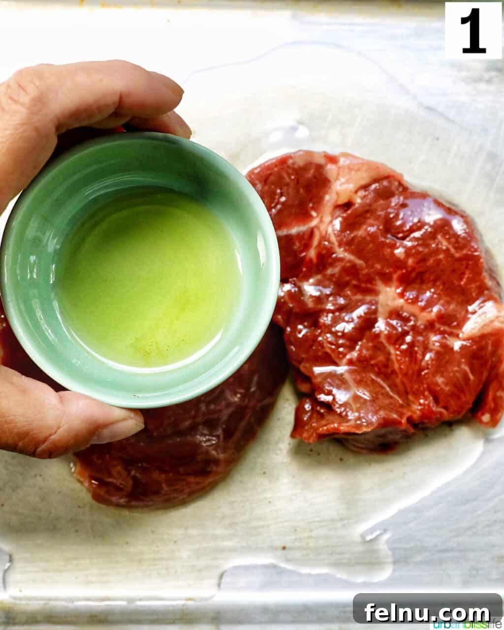Air Fryer Filet Mignon Perfection 6 a hand holding a bowl of olive oil, drizzling it over a raw filet mignon steak.