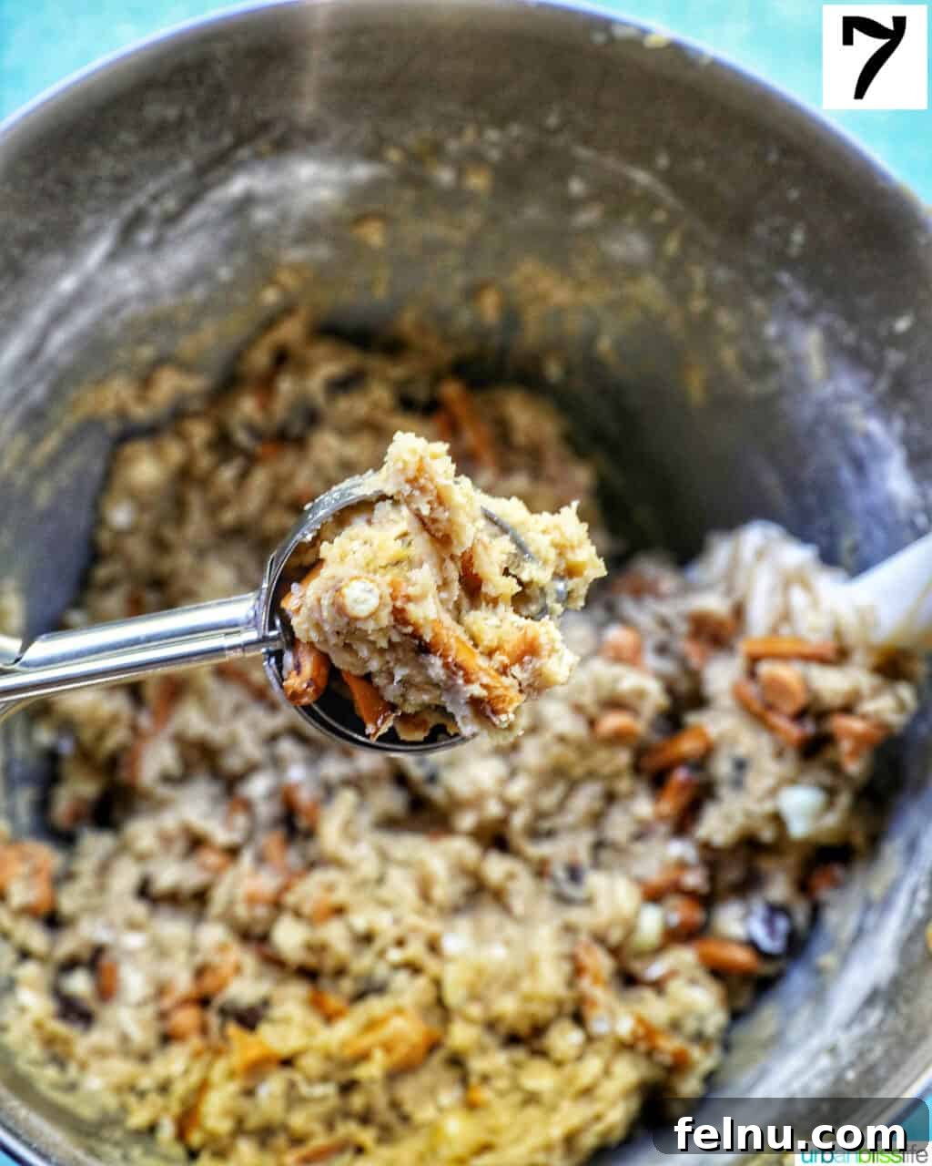 cookie scoop full of cookie dough over a stand mixer bowl full of cookie dough.