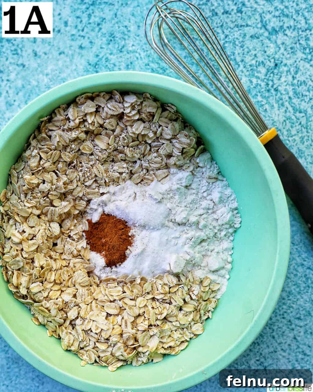 dry ingredients for cookie batter in a green bowl with whisk.