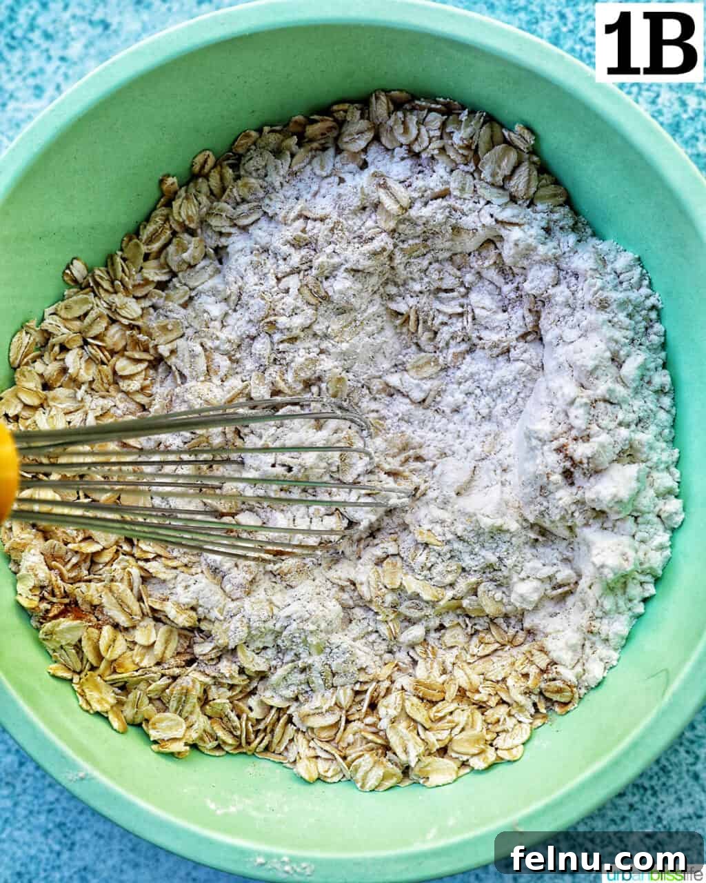 dry ingredients for cookie batter in a green bowl with whisk.