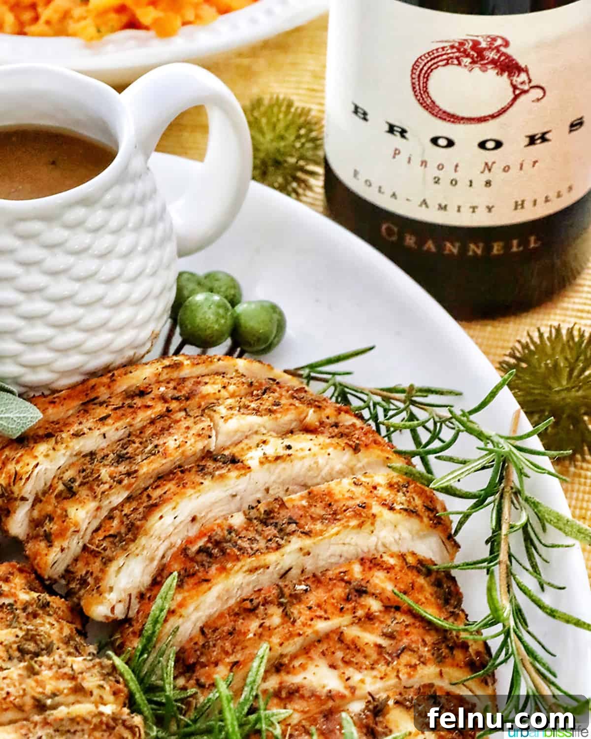 Crispy and Tender Air Fryer Turkey Breast 17 Sliced air fryer turkey breast on a plate, garnished with fresh herbs and lemon slices, with gravy and a bottle of wine in the background.