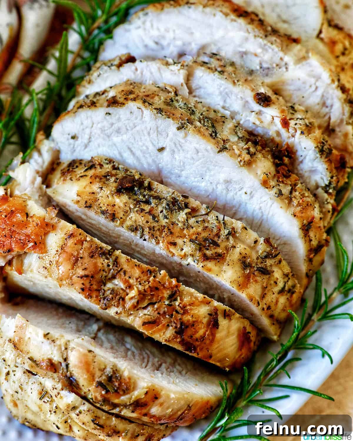 Crispy and Tender Air Fryer Turkey Breast 3 Close-up of succulent sliced turkey breast adorned with rosemary sprigs on a pristine white plate.