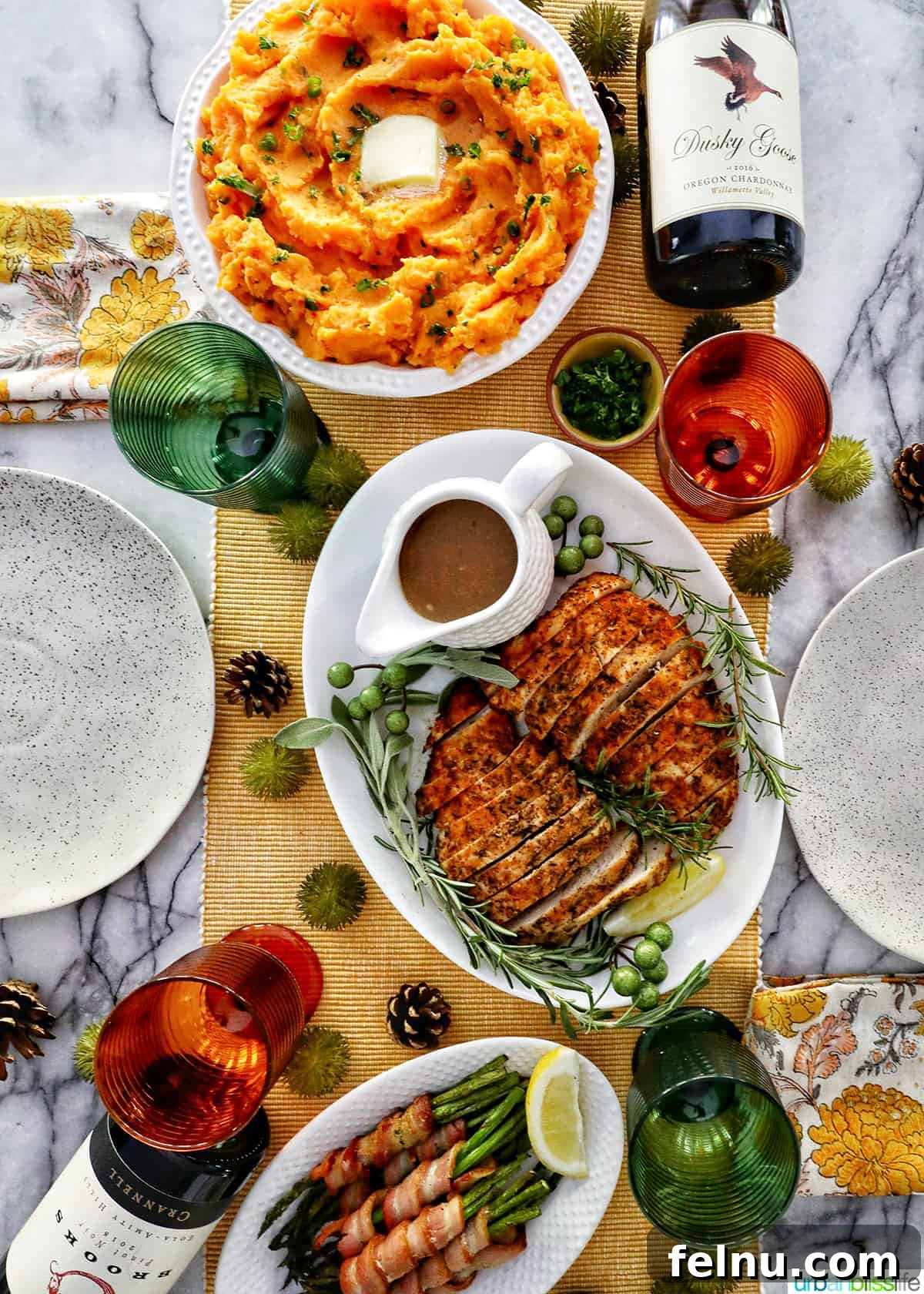 Silky Sweet Potato Puree 11 Thanksgiving dinner table with sliced turkey tenderloin, whipped sweet potatoes, bacon wrapped asparagus, bottles of wine, and servingware.