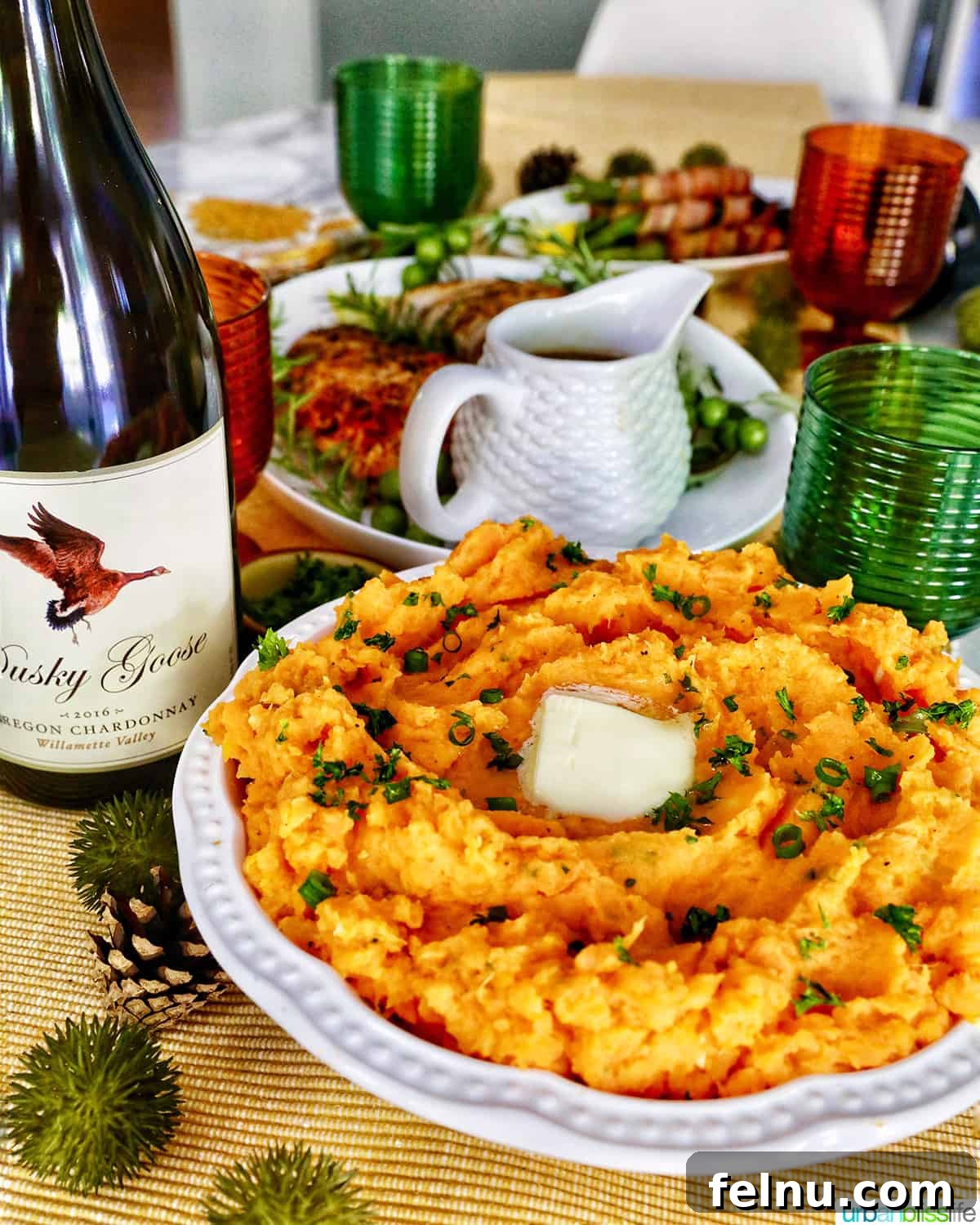 Silky Sweet Potato Puree 12 mashed sweet potatoes in a bowl in front of a bottle of dusky goose oregon Chardonnay and a table set for Thanksgiving.