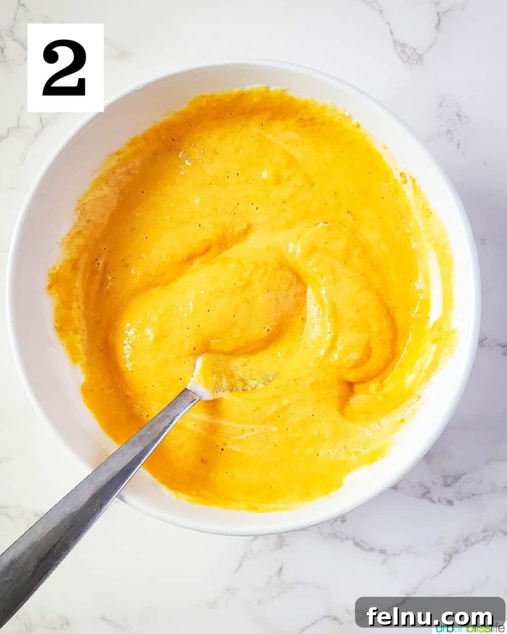 Easy Frozen Pumpkin Pupsicles 6 A spoon mixing the pumpkin puree and yogurt together in a bowl, creating a smooth, orange batter.