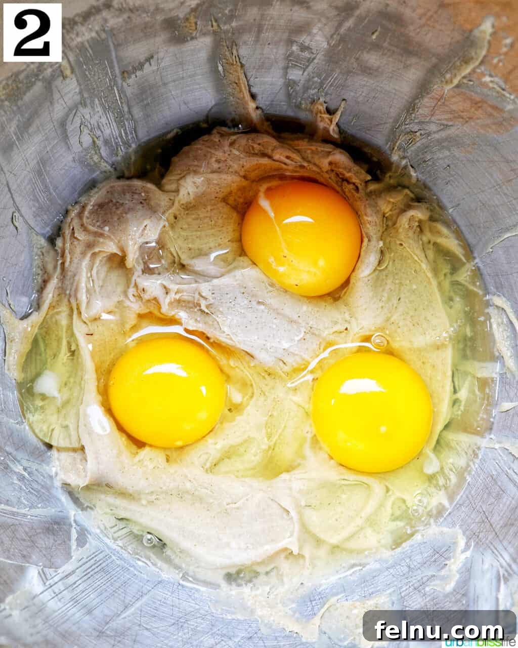 Eggs being added to the cinnamon pie batter in a stainless steel mixing bowl.