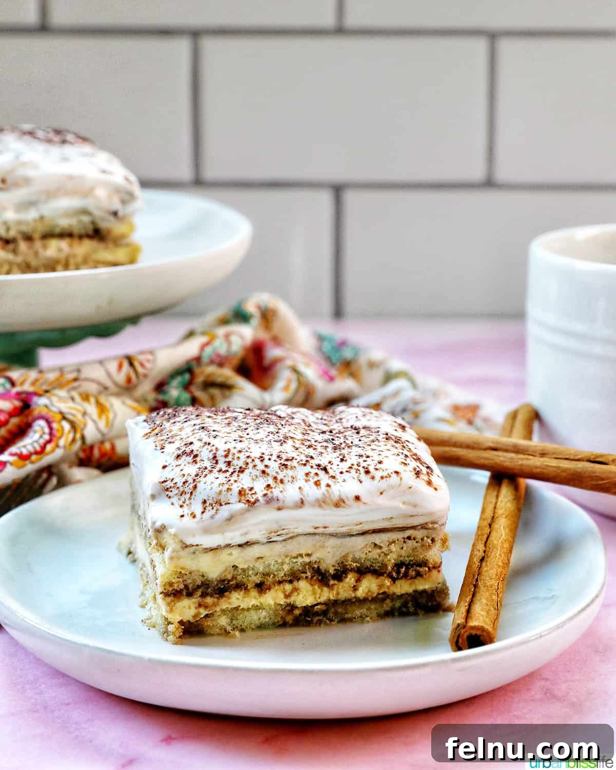 Decadent Dairy-Free Tiramisu 3 A single slice of dairy-free tiramisu on a white plate, elegantly positioned with a cup of coffee behind it.