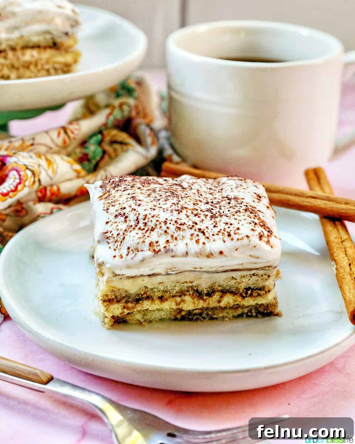 Decadent Dairy-Free Tiramisu 22 A mouth-watering slice of dairy-free tiramisu on a white plate, ready to be enjoyed, with a coffee cup in the background.