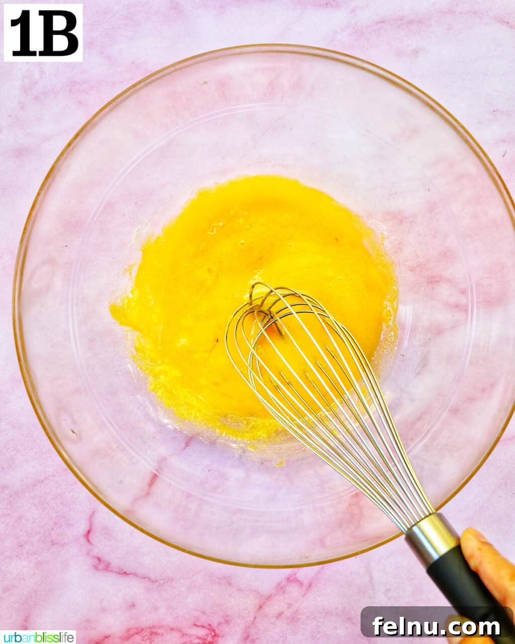 Decadent Dairy-Free Tiramisu 6 A whisk vigorously beating egg yolks in a clear glass bowl to achieve a creamy consistency.