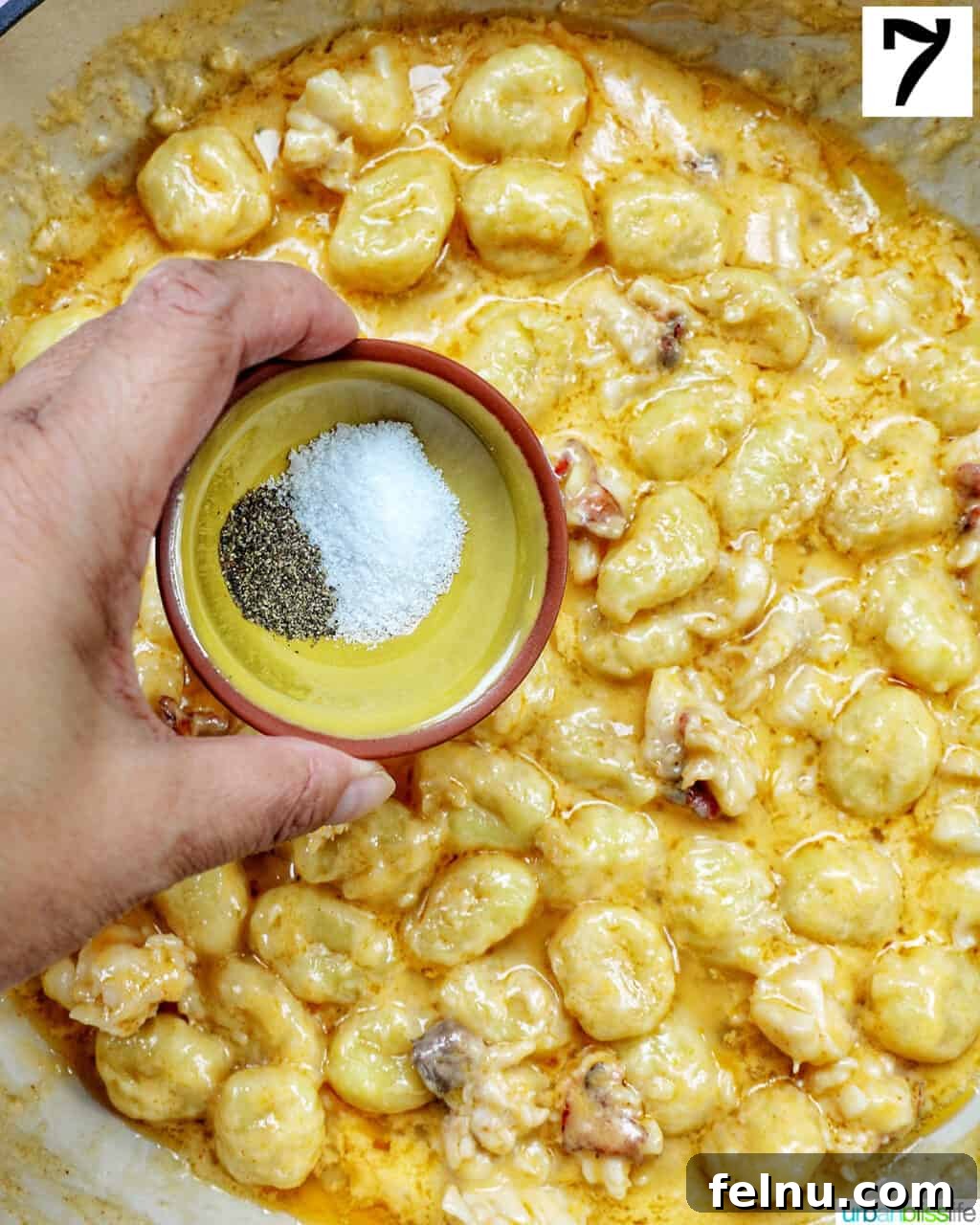 Decadent Lobster Gnocchi 11 A hand seasoning lobster gnocchi with salt and pepper in a skillet.