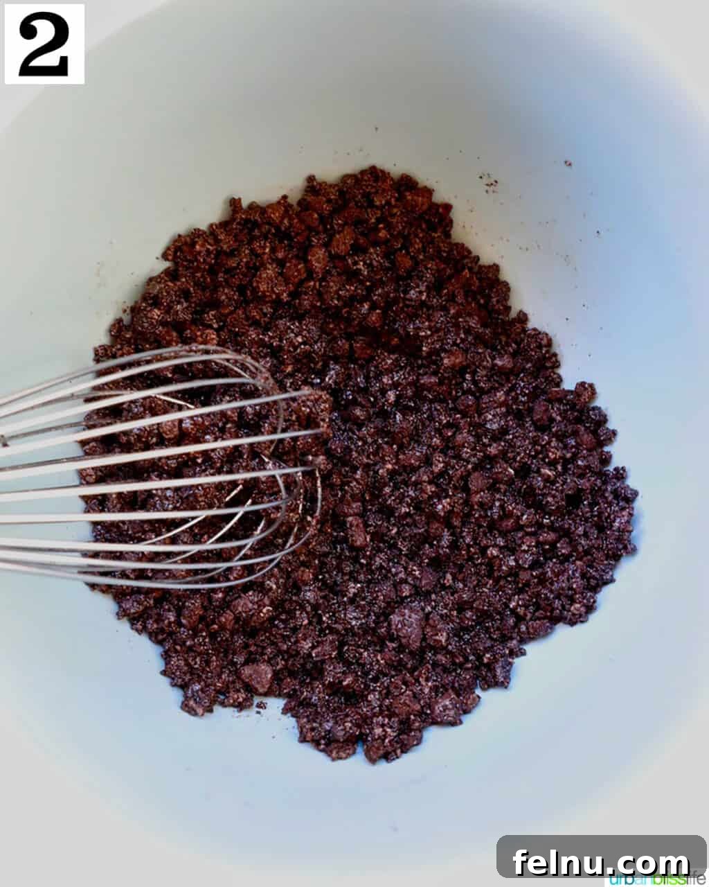 Cool Mint Chocolate Indulgence 6 A whisk thoroughly combining crushed Oreos and melted butter in a bowl, forming a uniform pie crust mixture.