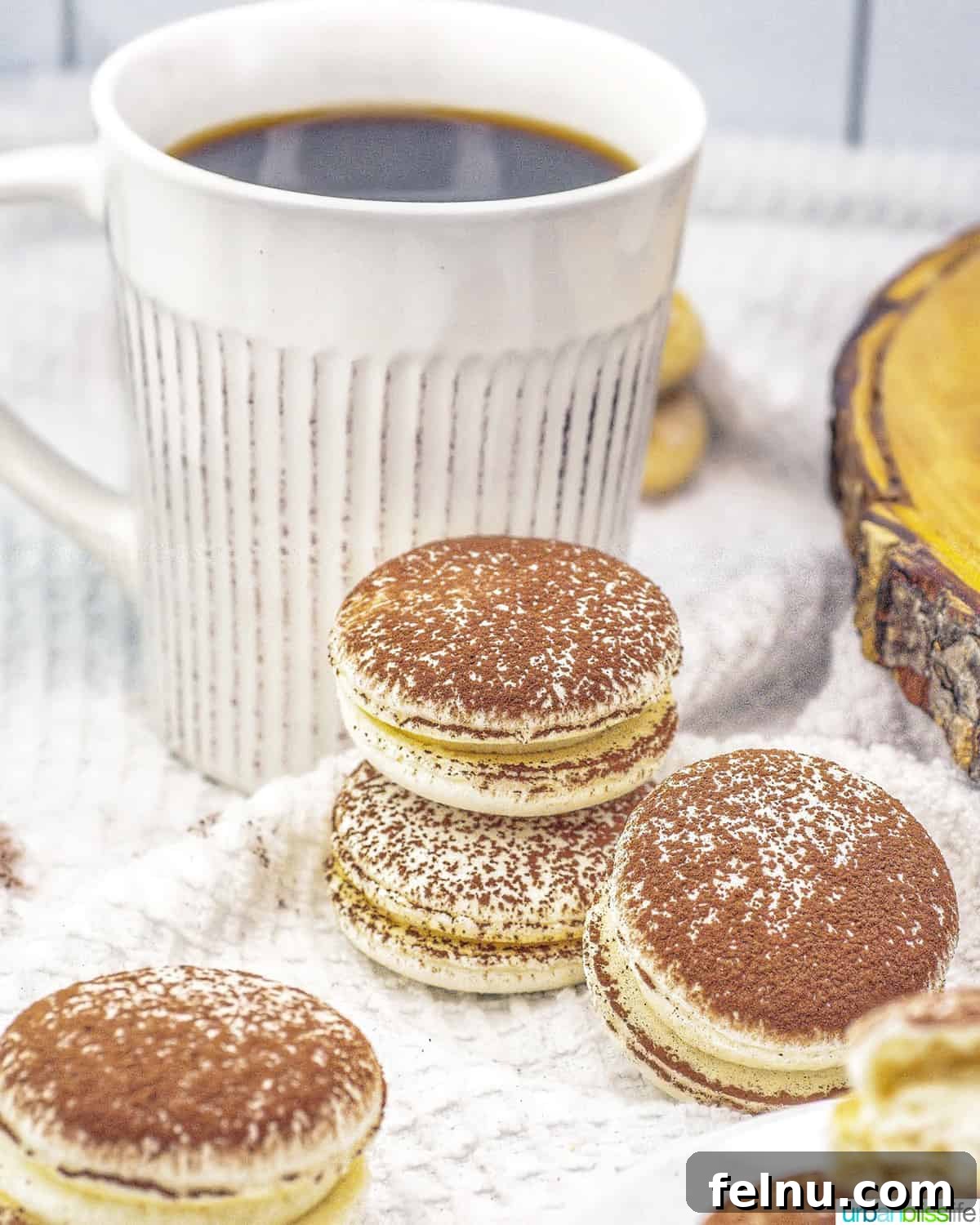 Espresso Mascarpone Macarons 22 Stacks of tiramisu macarons elegantly arranged next to a steaming cup of coffee.