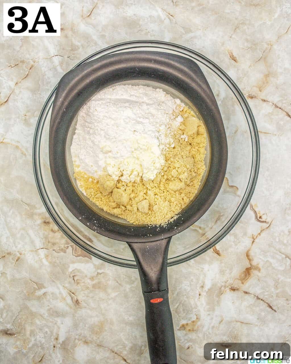 Espresso Mascarpone Macarons 8 Dry ingredients being sifted through a fine mesh sieve into a glass bowl.