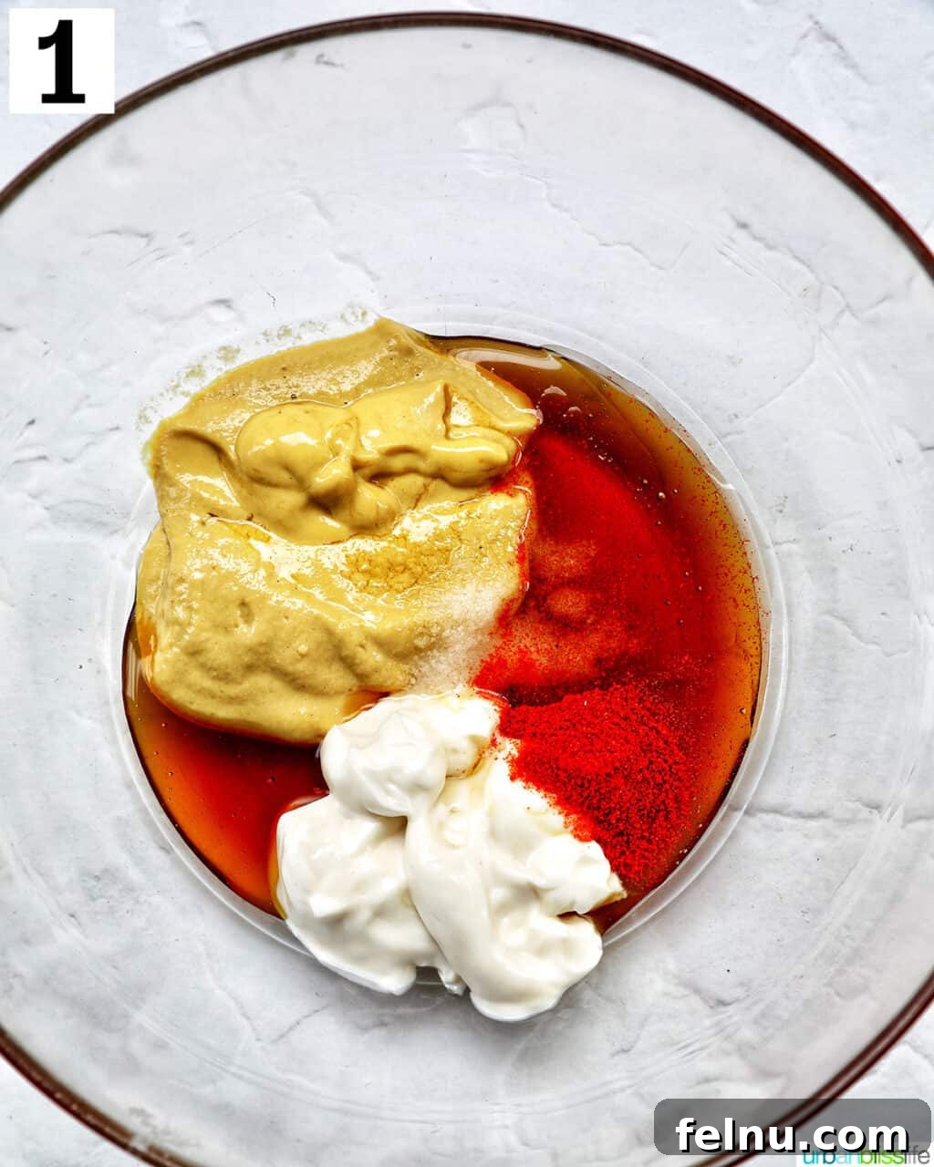 clear glass bowl with ingredients to make hand dipping a chicken tender into a bowl of honey mustard dipping sauce.