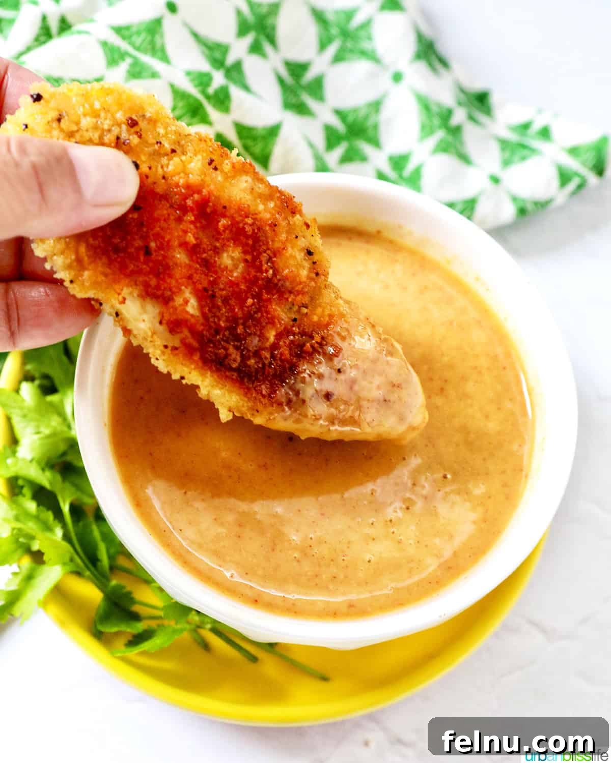 hand dipping a chicken tender into a bowl of honey mustard dipping sauce.