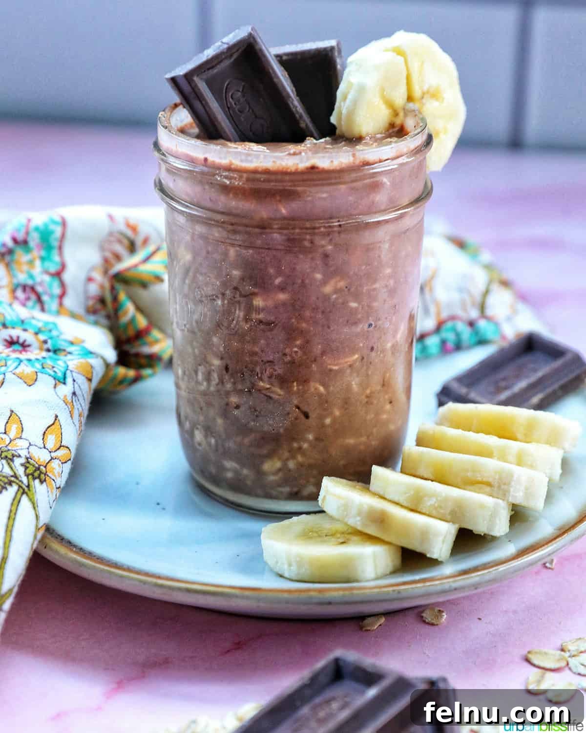 Chocolate Protein Power Oats 3 Chocolate protein overnight oats in a glass and on a plate, topped with banana slices and chocolate pieces.