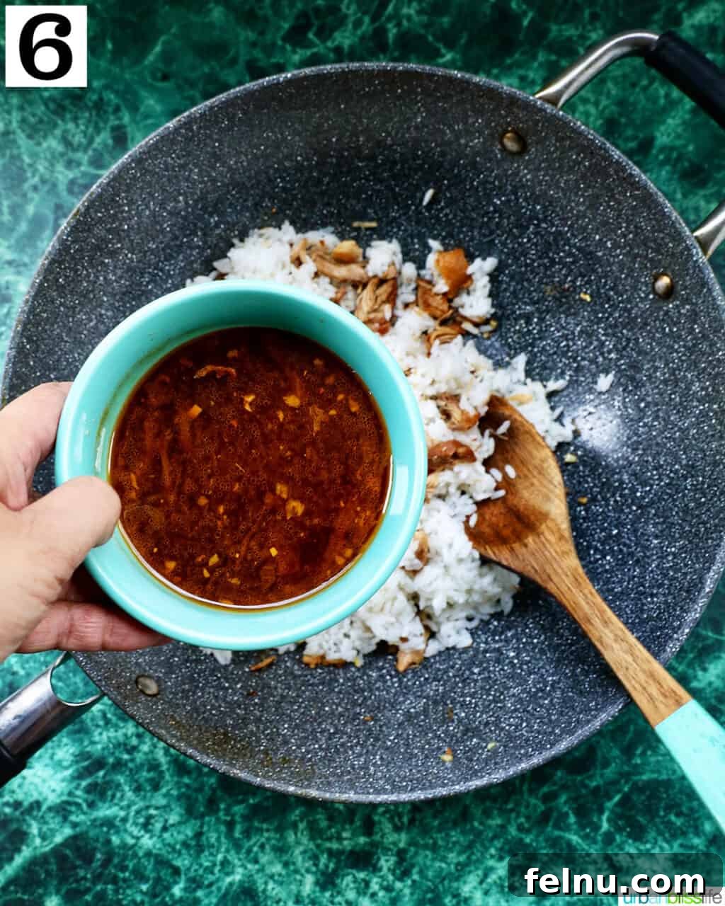 Savory Garlic Adobo Fried Rice 10 A hand adding adobo sauce to the wok, where adobo chicken and rice are being stirred with a wooden spoon.