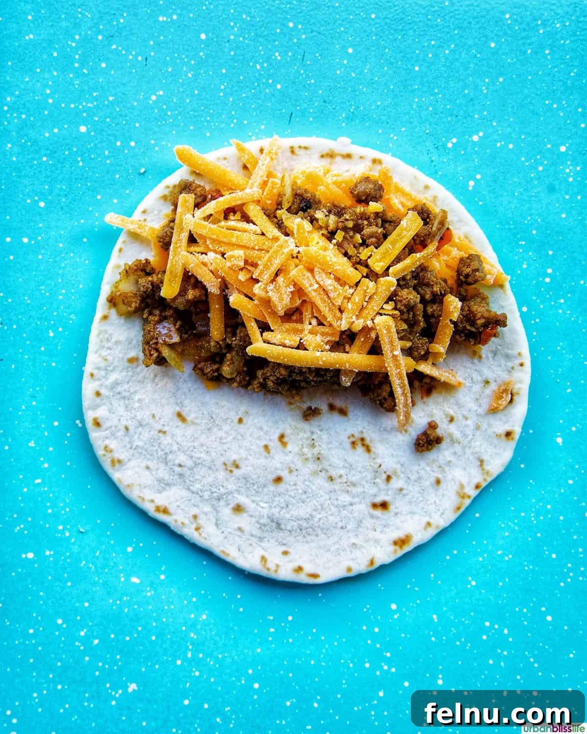 Golden-Crisp Beef Tacos 13 More shredded cheese sprinkled over the ground beef mixture on a tortilla.