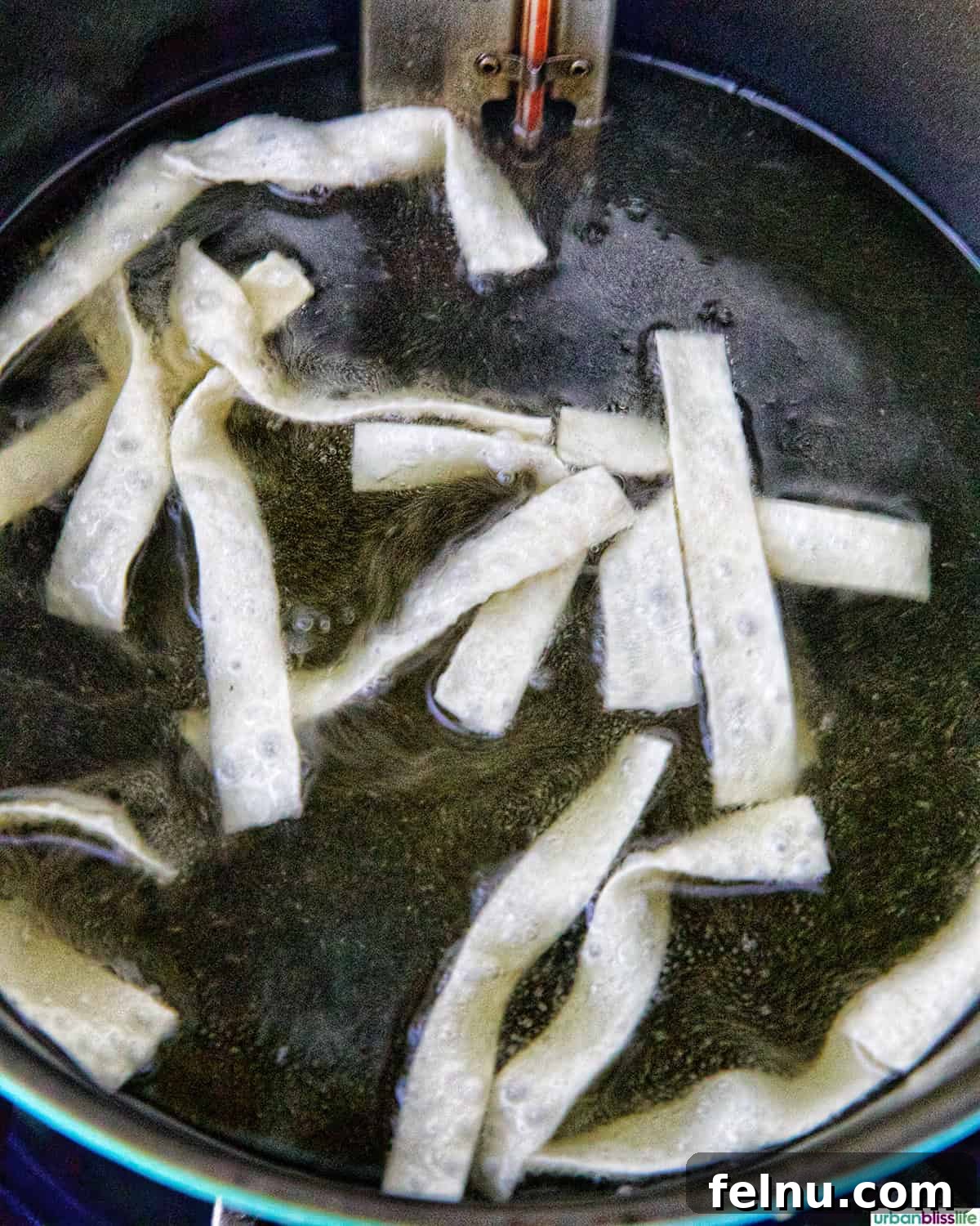 Wonton strips bubbling and turning golden in hot oil, indicating they are actively frying.