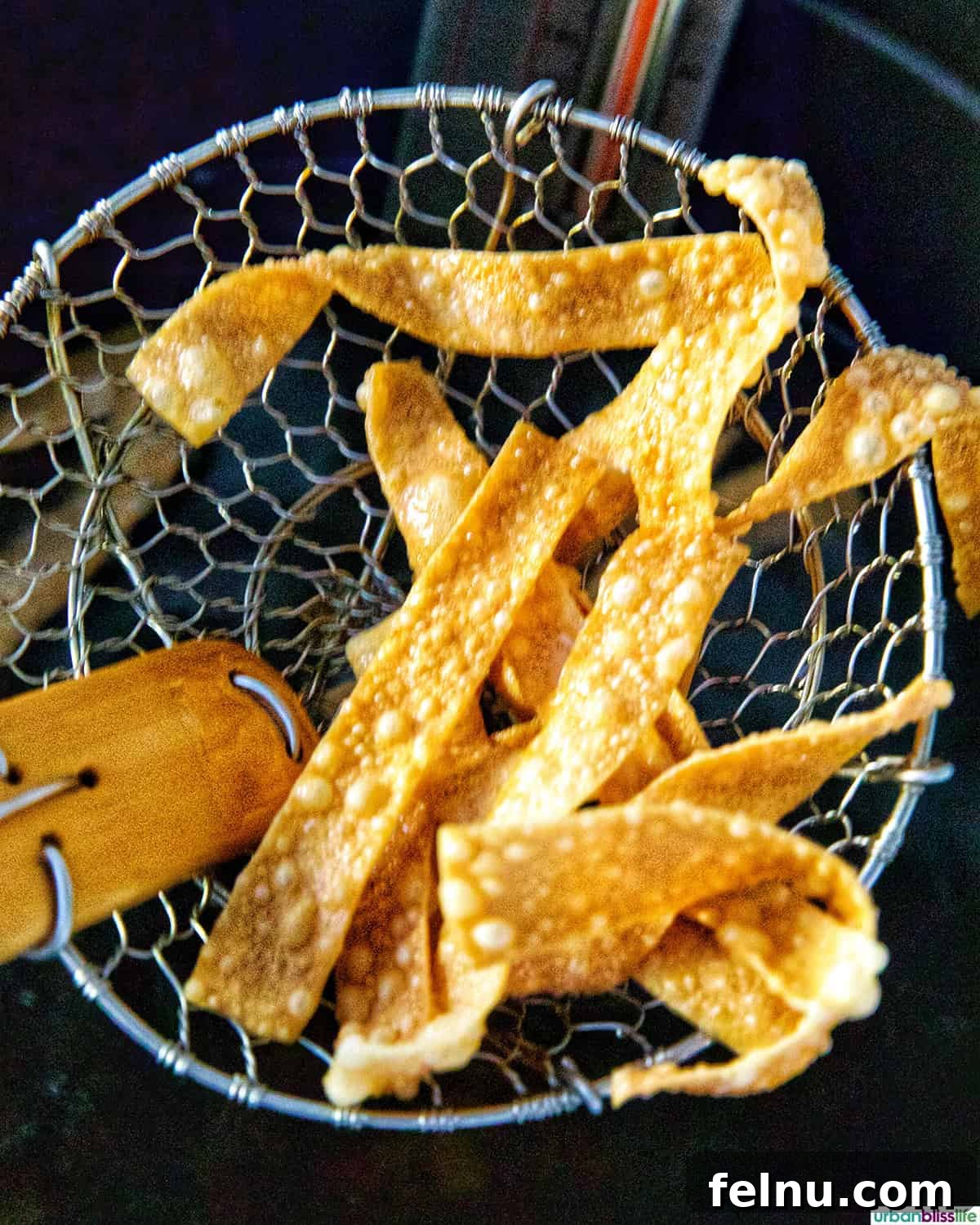 A spider strainer lifting freshly fried wonton strips from the hot oil, allowing excess oil to drain.