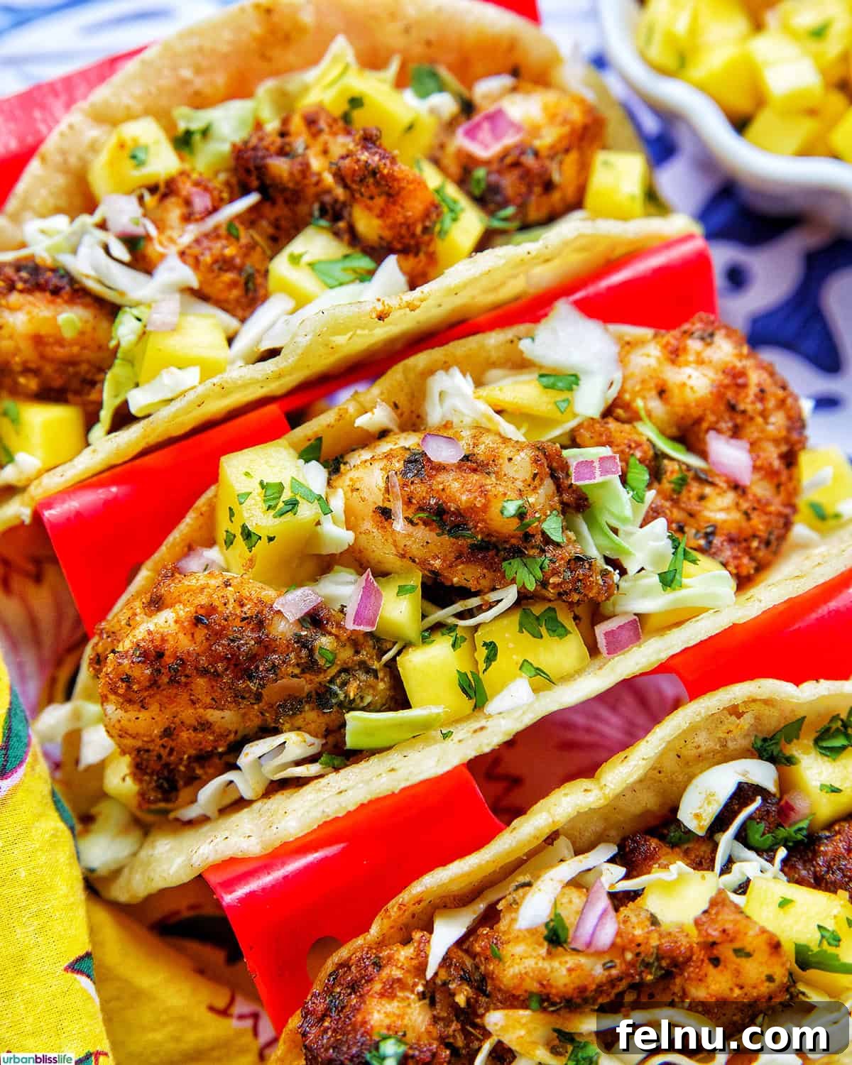 Three perfectly cooked air fryer shrimp tacos arranged appealingly in a red taco stand, ready to be enjoyed.