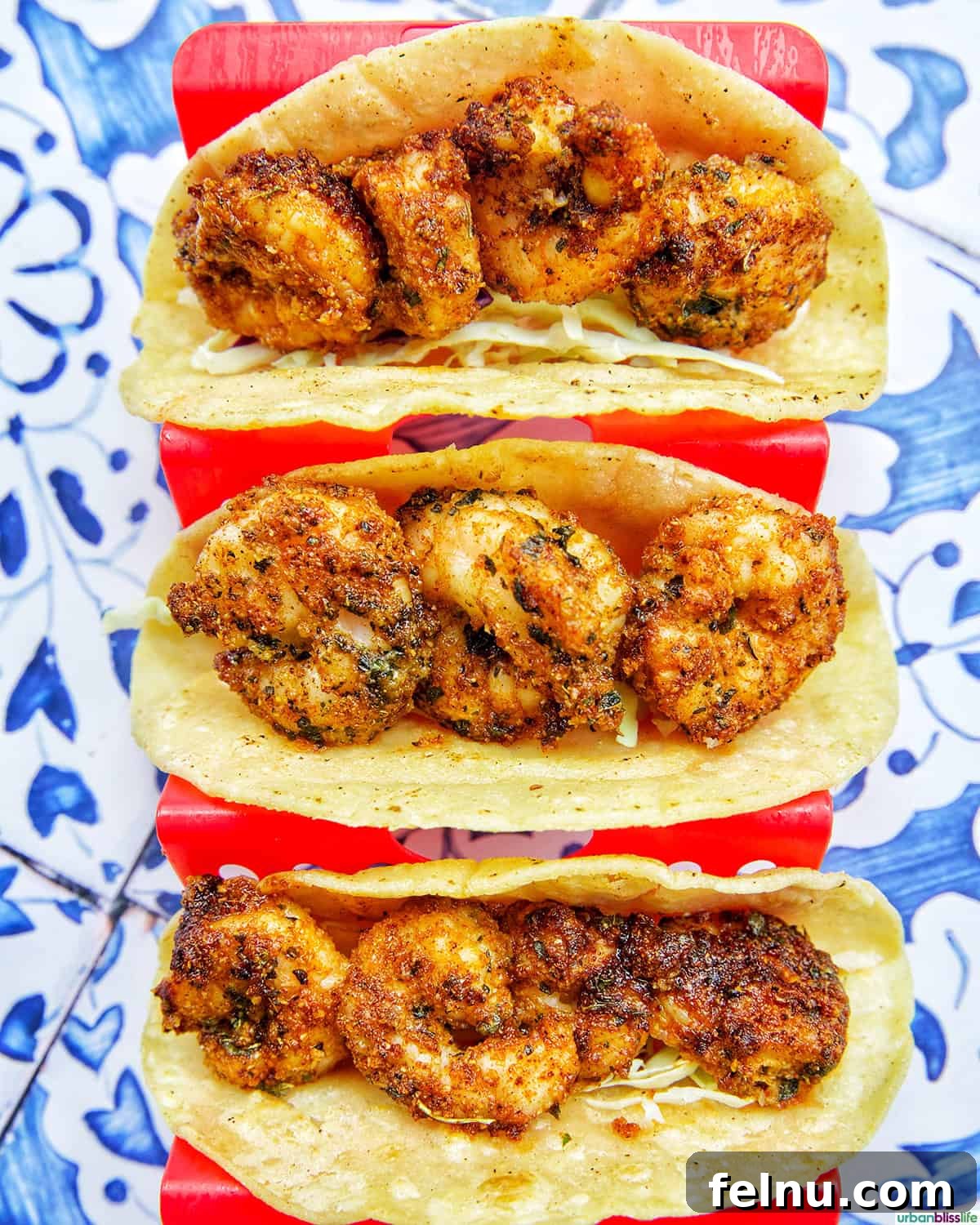 Three air fryer shrimp tacos, filled with shrimp and cabbage, in a red taco stand, ready for toppings.