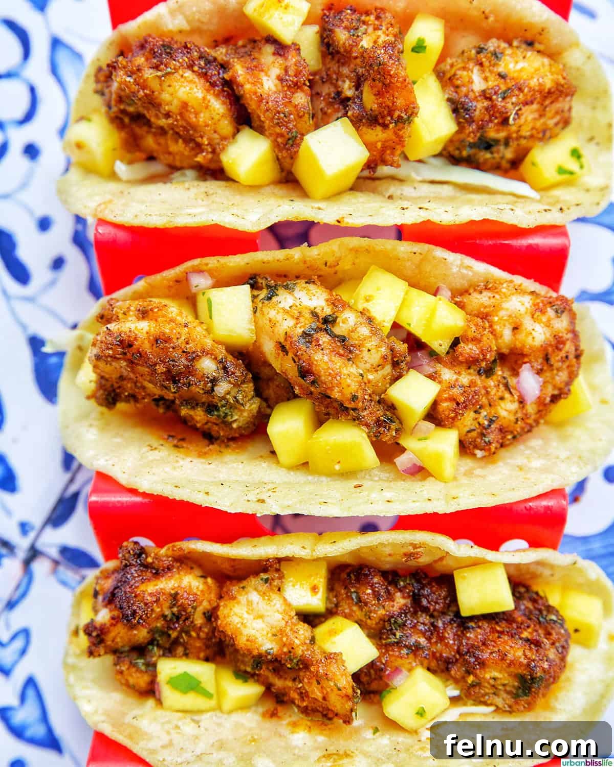Three fully assembled air fryer shrimp tacos, topped with mango salsa, in a red taco stand.