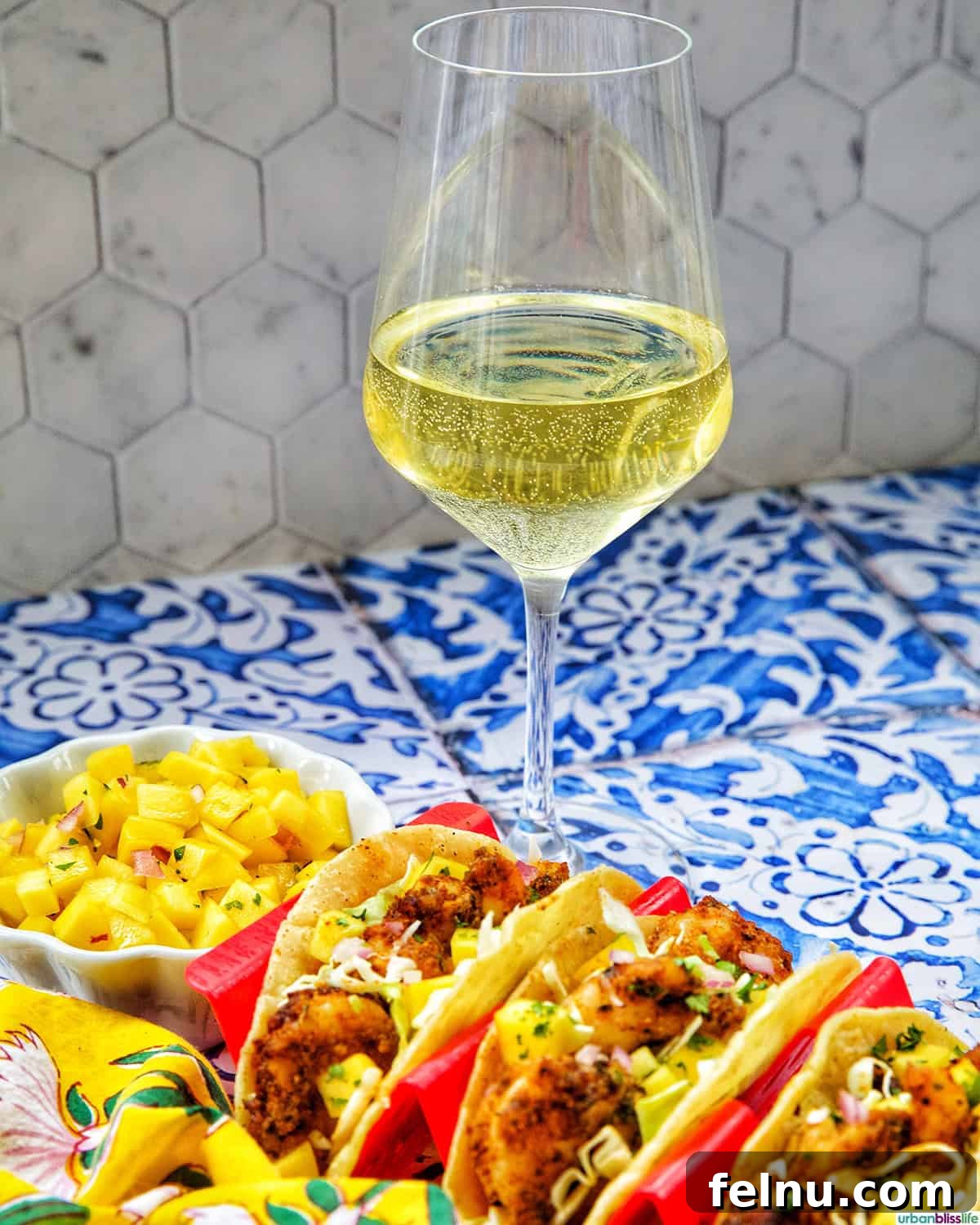 A glass of chilled white wine elegantly placed next to three air fryer shrimp tacos, suggesting a perfect pairing.