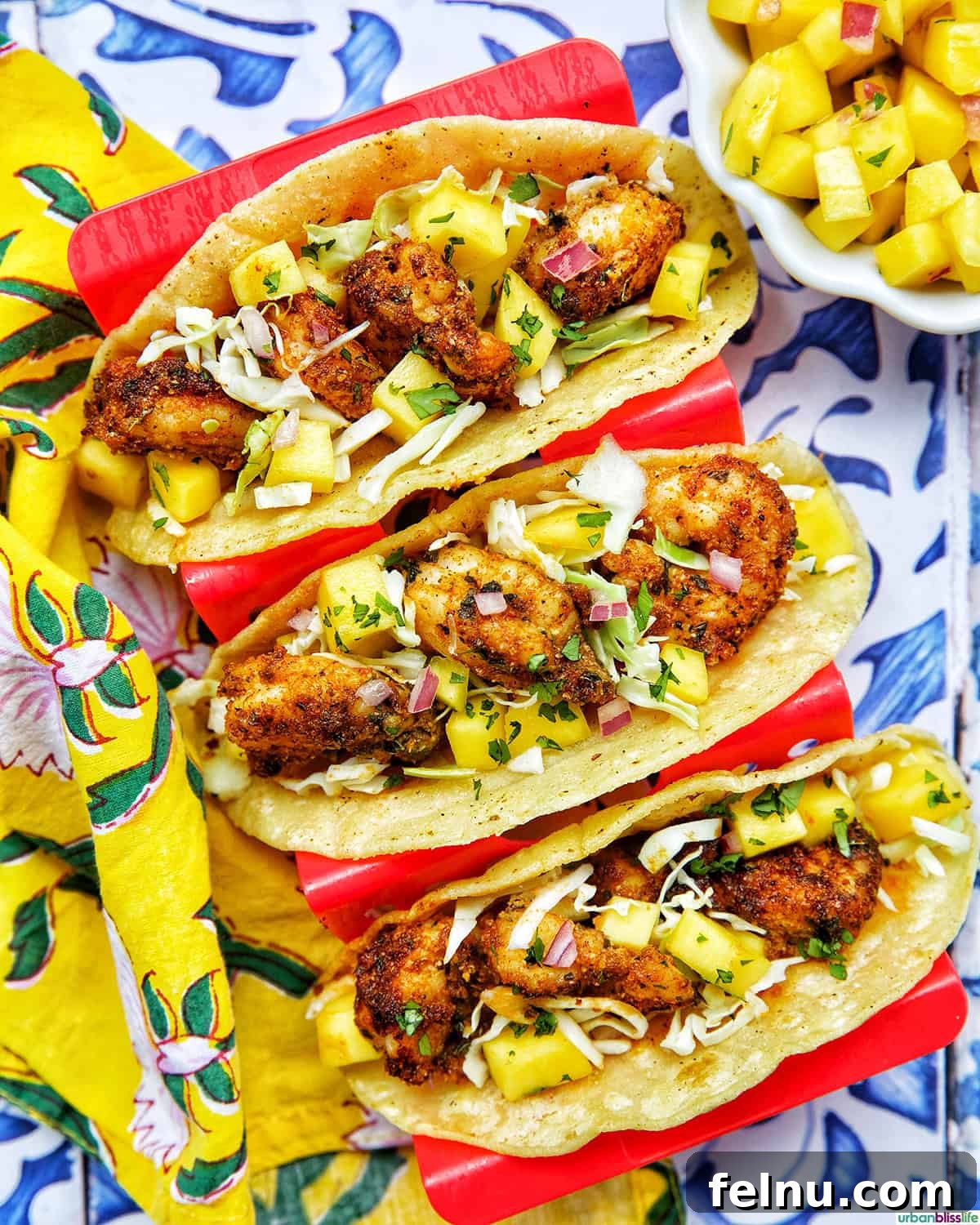 Three air fryer shrimp tacos in a red taco stand, beautifully plated with a vibrant side of mango salsa.