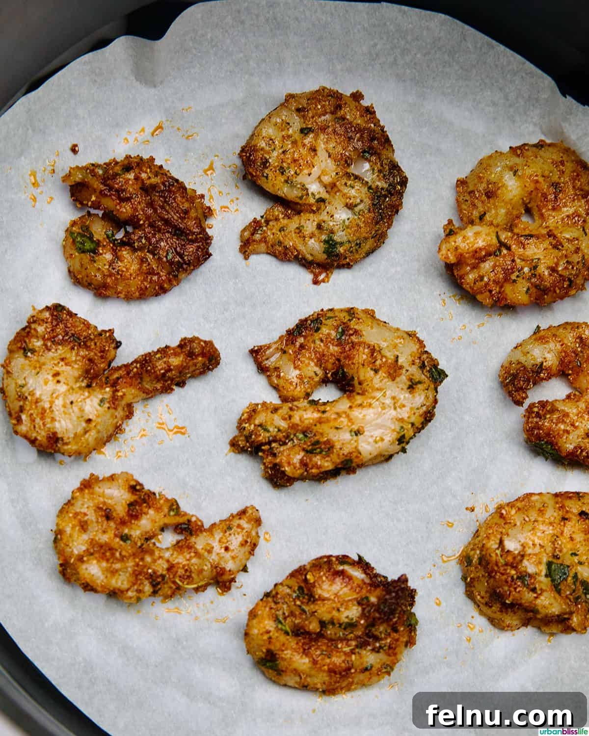Seasoned shrimp arranged in a single layer on parchment paper in an air fryer basket.