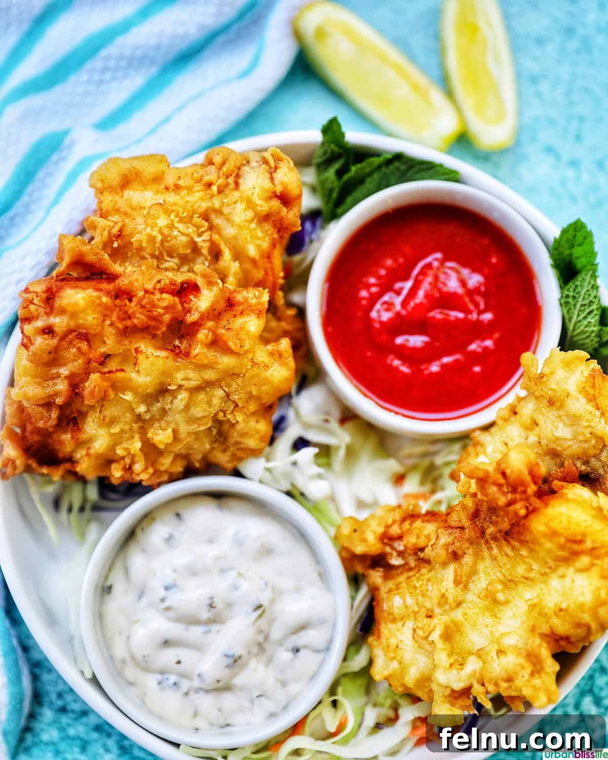 Crispy Air Fryer Cod with Lemon Garlic Butter 2 air fryer cod pieces on a plate with sides of tartar sauce, coleslaw, and cocktail sauce.