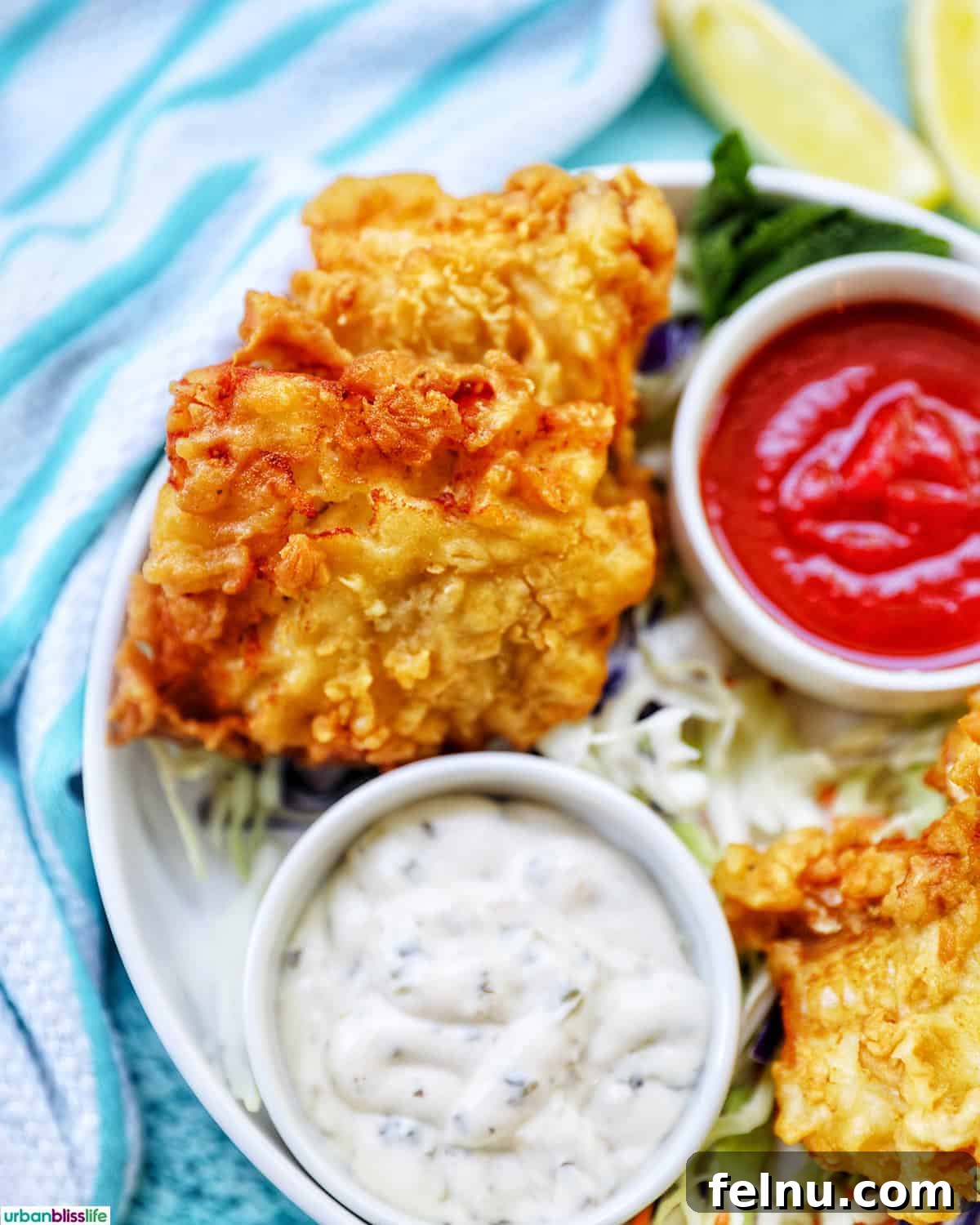 Crispy Air Fryer Cod with Lemon Garlic Butter 11 air fryer cod pieces on a plate with sides of tartar sauce, coleslaw, and cocktail sauce.